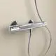 Thermostatischer Brausearmatur von Ideal Standard, montiert an einer hellen Wand, mit einem Steuerknopf und einem flexiblen Duschschlauch.